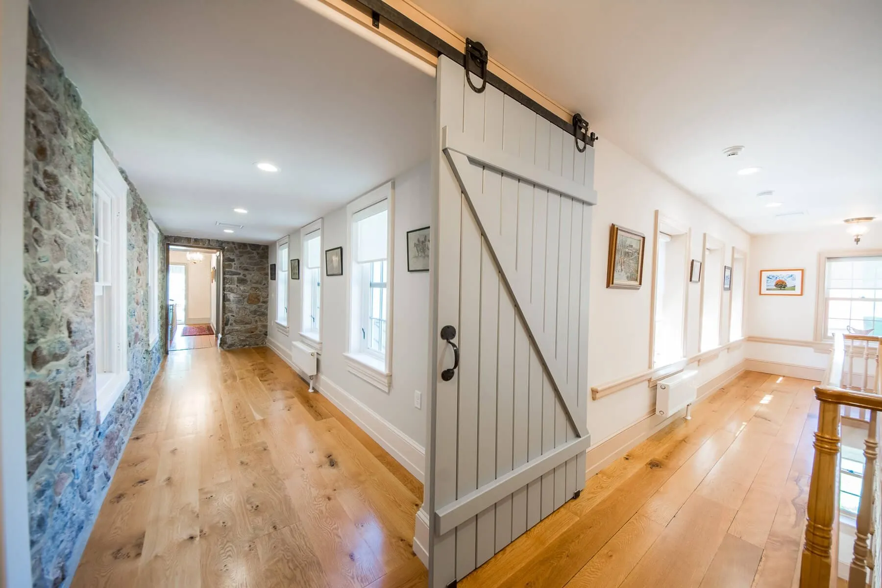 Restored home hallway with a stone wall, wide-plank oak floors, and a white sliding barn door — cover image for the Bedwell Custom Builders website project