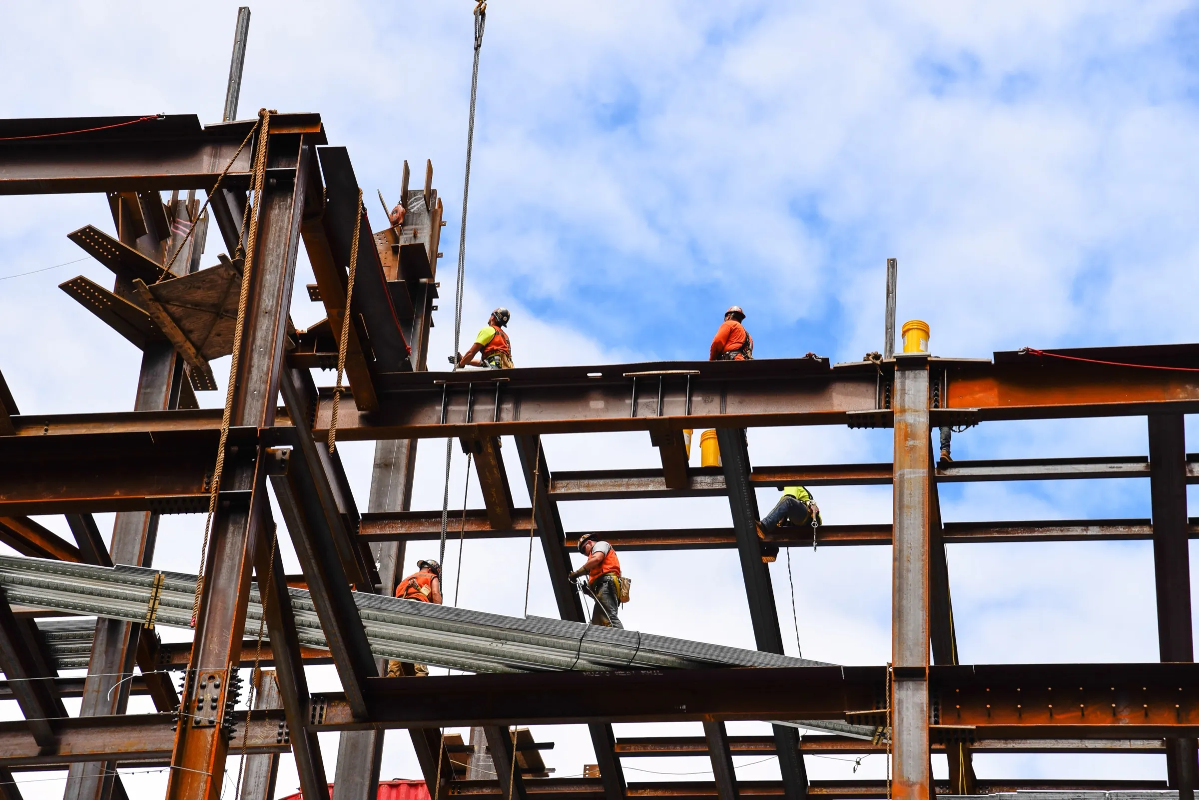 Ironworkers in hard hats and hi-vis vests working across the steel frame of a building under construction