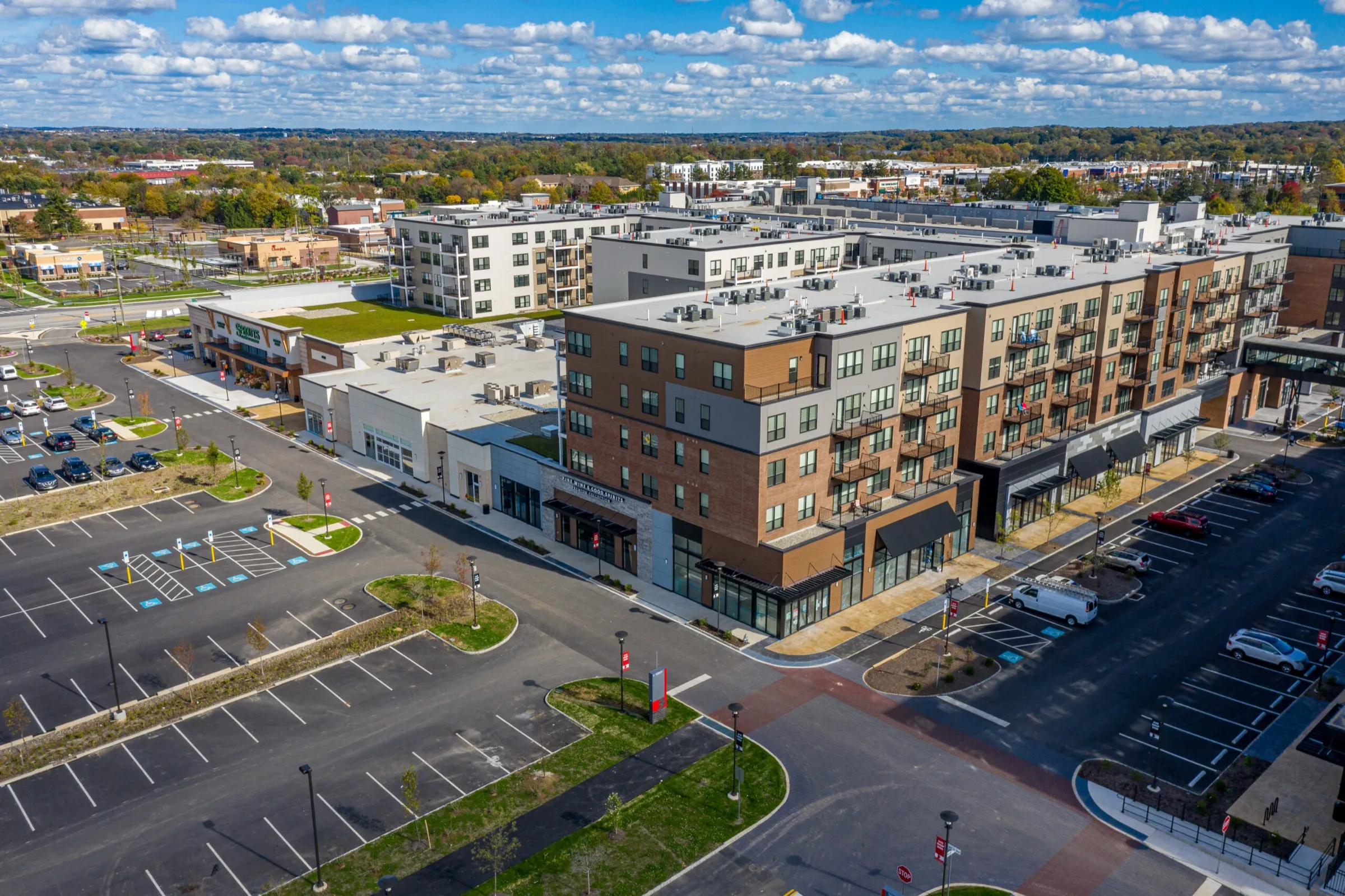 Aerial view of a new brick mixed-use development with ground-floor retail, landscaped parking lots and surrounding streets — cover image for the Gilmore & Associates website project