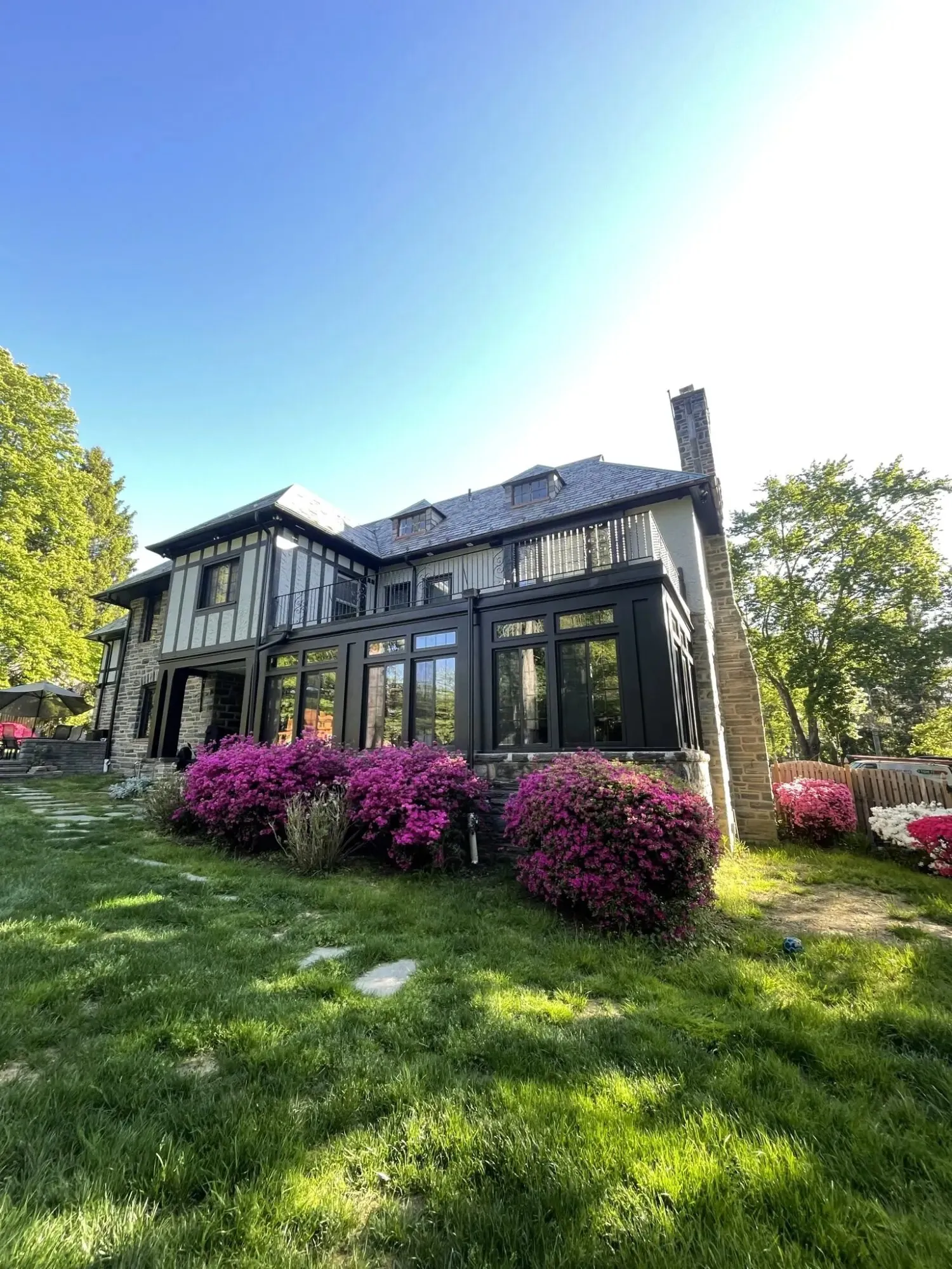 Stone-and-shingle home with large black-framed windows, blooming azaleas, and a green lawn under a blue sky — cover image for the Mulroy Bay Builders website project