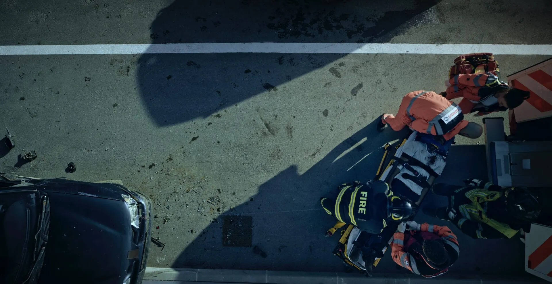 Overhead view of firefighters and paramedics loading an injured person onto a stretcher beside a crashed car — cover image for the Techline Trauma website project