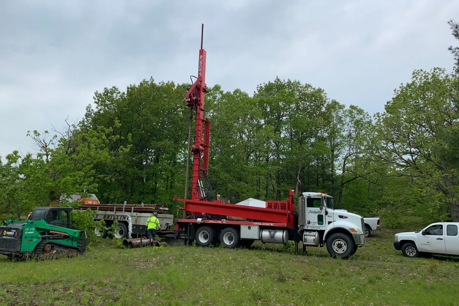 Red sonic drill rig mounted on a truck at a wooded field site, a crew member in a high-visibility vest working beside it — cover image for the Weston Solutions website project