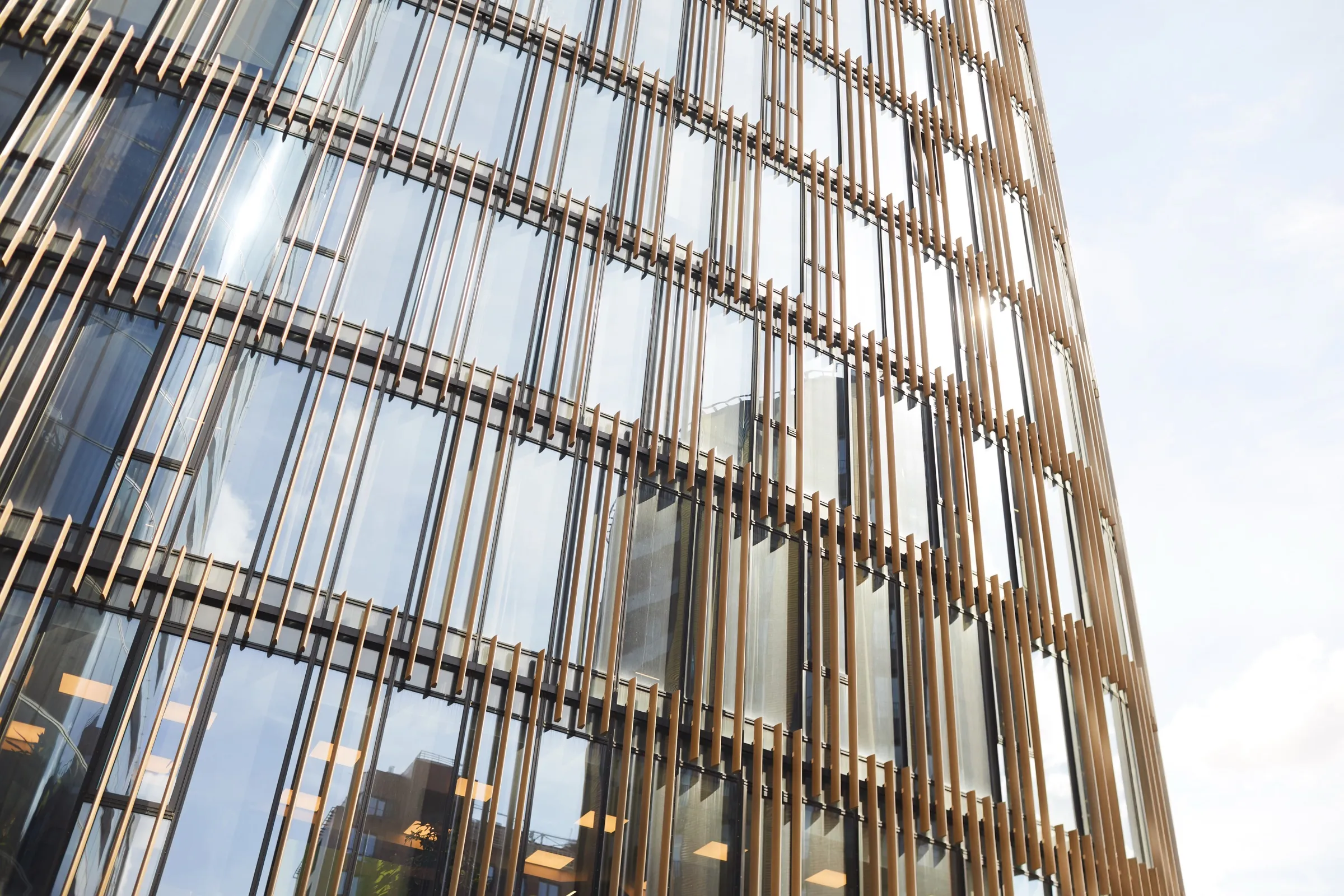 Glass office tower wrapped in vertical copper-toned fins, viewed from street level
